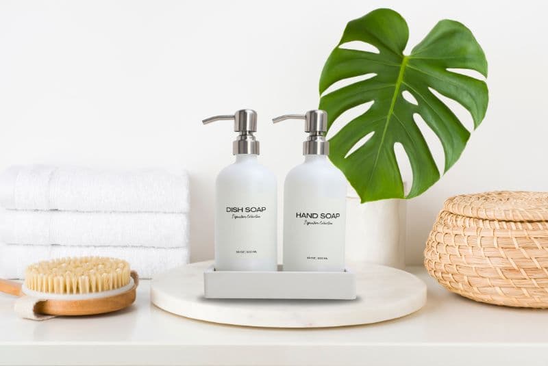 Frosted dish soap and hand soap pumps styled with towels, a bath brush, and a monstera leaf.